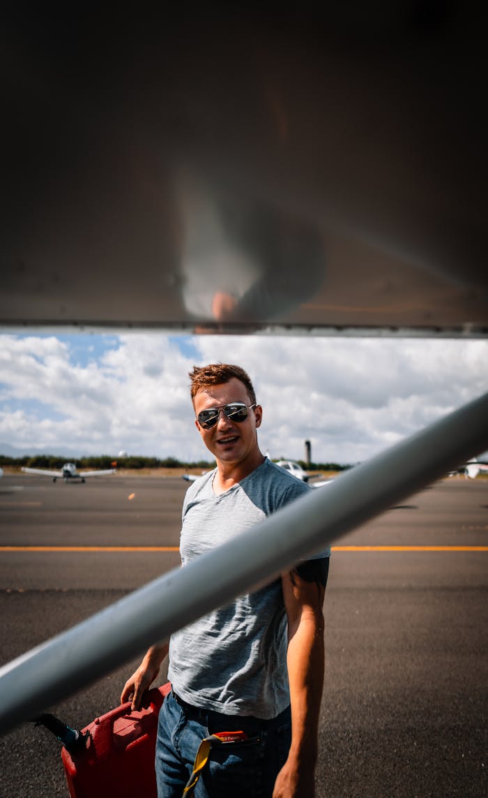Content young male in casual wear and sunglasses with red fuel can standing near modern jet in aerodrome